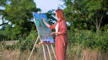 Yaratıcı hobi, yetenekli kadın sanatçı ağaçların arka planında yaratıcı bir tablo çiziyor.