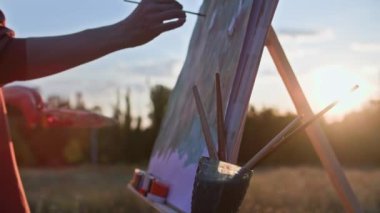 Yaratıcı bir hobi, yetenekli bir kadın sanatçı parktaki sehpayı güneş ışığına karşı kullanarak resim çizer.