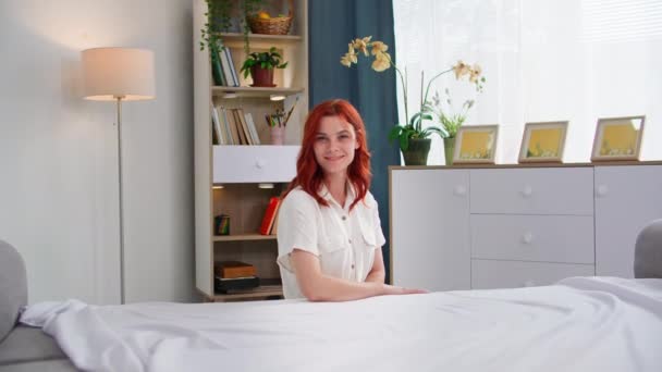 寝室で寝た後 ベッドを掃除している若い赤毛の女性の肖像画 笑顔とカメラを見る — ストック動画