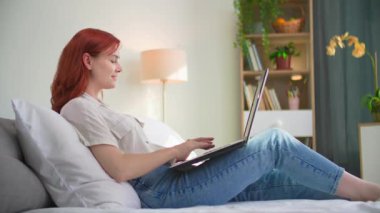 Kadın serbest çalışan, odada yatarken uzaktan internet ve dizüstü bilgisayar kullanıyor.
