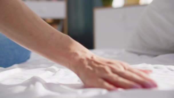 若い女性はベッドの上に座っている間 朝の睡眠の後のクリーン ベッドのリネンを通して手を動かします クローズアップ — ストック動画