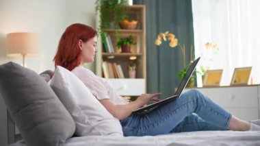 Uzaktan kumandalı iş, kadın çalışan yatakta yatarken internet ve laptop kullanıyor.