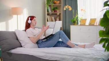 Çevrimiçi iletişim, video görüşmesinde konuşan genç bir kadın evdeki kanepede dinlenirken kulaklık kullanıyor.