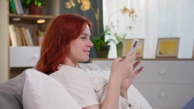 Güzel bir kadın evde dinlenirken sosyal ağlarda arkadaşlarıyla iletişim kurmak için akıllı telefon kullanır.
