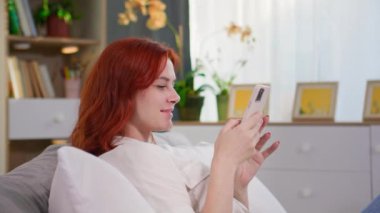 Genç ve güzel bir kadın yatakta yatarken akıllı telefon kullanır ve haberleri okur veya arkadaşlarıyla mesajlaşır.