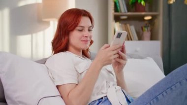 Genç, güzel bir kadın internette haberlere bakıyor. Odada yatarken cep telefonu kullanıyor.
