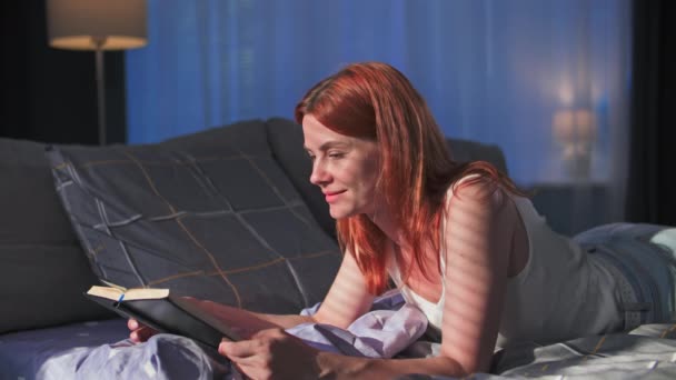在家里休息 年轻迷人的女人躺在床上看书 在家里休息 — 图库视频影像