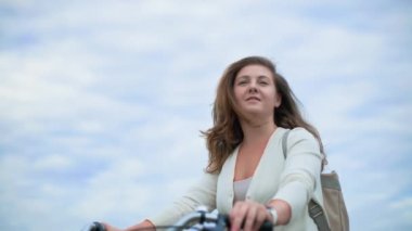 Aktif eğlence, genç ve güzel bir kadın şehir dışında mavi gökyüzüne karşı bisiklet sürüyor.
