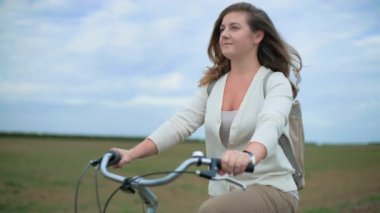 Güzel genç bir kadın bir tarlanın ortasında bisiklet sürüyor ve gökyüzüne bakıyor.