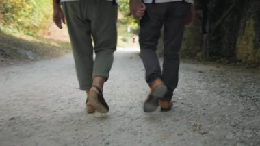 Aktif emekliler, yaşlı karı koca, güneşli bir günde yol boyunca el ele yürürler.