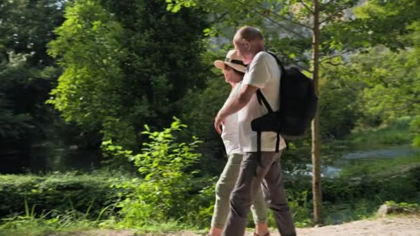 在一个阳光明媚 温暖的天气里 一群身披背包 精力充沛的老年男女游客在公园里沿着小河散步 玩得很开心 — 图库视频影像