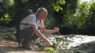 Emeklilik hayatı, sırt çantalı yaşlı bir adam güneşli bir günde, sıcak bir parkta otururken, nehirde yürümekten ve yüzünü yıkamaktan zevk alır.
