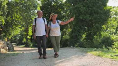 Emeklilik seyahati, neşeli yaşlı adam ve kadın birlikte tatilin tadını çıkarıyorlar ve güneşli bir günde parkta el ele yürüyorlar.