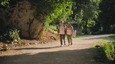 Emeklilik hayatı, aktif yaşlı kadın ve erkek emekliler birlikte güzel manzaranın tadını çıkarıyorlar ve sıcak bir günde birlikte seyahat ederken parkta dolaşıyorlar.