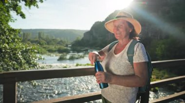 Elinde bir şişe suyla çekici bir bayan turist sıcak bir günde parkta yürürken bir yudum alır.
