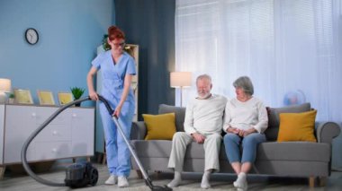 Yaşlı, kadın sosyal hizmet görevlisi ev işleri ve süpürge odası olan yaşlı bir çifte yardım ediyor, gülümsüyor ve kameraya bakıyor.