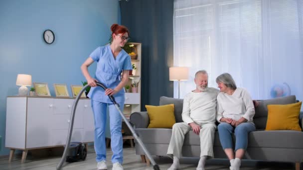 在养老院 穿着医疗制服 手里拿着吸尘器的社会工作者帮助一对老年夫妇打扫房间 — 图库视频影像