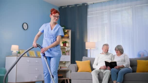 社会工作者 穿着西服 手里拿着吸尘器的年轻女性清扫着老年人的房间 — 图库视频影像