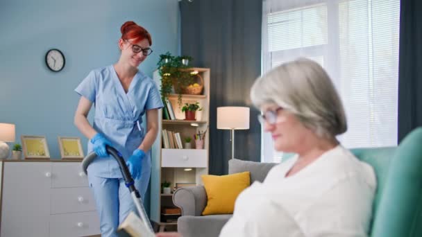 退休人员的社会保护和护理 女性社会工作者用吸尘器帮助一位孤独的老年妇女清理公寓的地板 — 图库视频影像