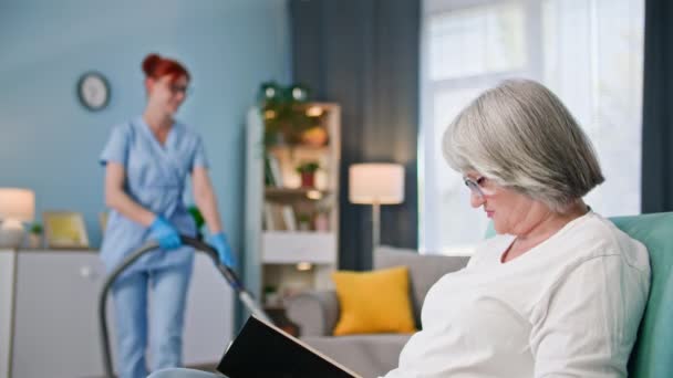 为老年人提供社会关怀 穿着医疗制服的女保姆帮助一位老年妇女在房间里打扫房间和清理地板 — 图库视频影像