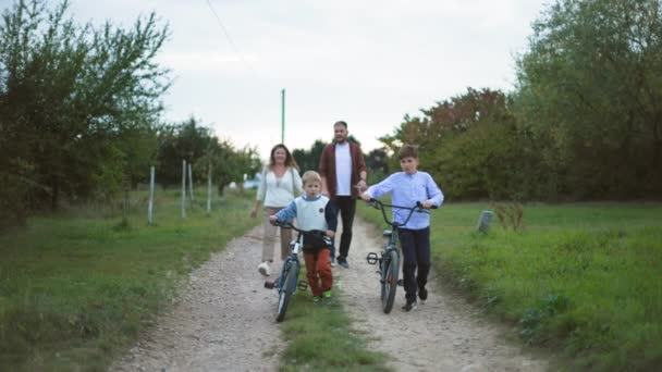 家族の週末 若い幸せな男性と女性の両親 子供が楽しんでいる間 街の外の田舎を歩いている自転車に乗っている — ストック動画