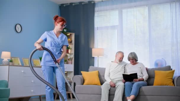 帮助穿着医疗制服 手里拿着吸尘器的老年女性社会服务人员帮助一位老年男女打扫公寓 — 图库视频影像