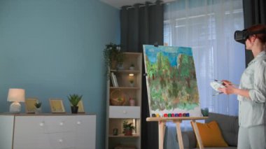 Büyütülmüş gerçeklik, modern yaratıcı kadın sanatçı sıcak bir odada dururken tuvale resim çizmek için viar gözlük kullanıyor.