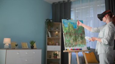 Hobiler ve modern teknolojiler, Viar gözlüklü genç bir yaratıcı kadın sanatçı, konforlu bir odada dikilirken artırılmış sanal gerçeklik kullanarak boya ve fırçalarla resim çizer
