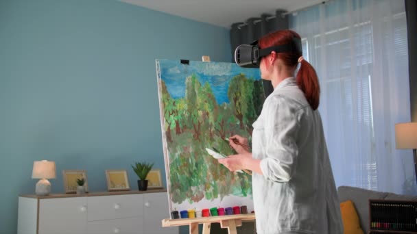 モダンアート クリエイティブな女性アーティストは居心地の良い部屋に立っているバイアグラスのペンキとブラシを使用してキャンバス上の絵を描きます — ストック動画