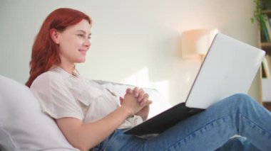 Güzel, gülümseyen bir kadın internette ya da yatakta yatarken online bir mağazada sayfaları karıştırıyor.