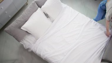 Genç ev hanımı rahat bir odada yattıktan sonra yatağını temizliyor.