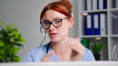 Çevrimiçi tıp, kulaklık takmış çekici genç bayan doktor hastane ofisinde dizüstü bilgisayarla hastaya danışmanlık yapıyor.