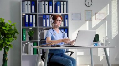 Genç bayan doktor hastalara kulaklık ve video iletişimini bilgisayardan, hasta kabul ederken tıbbi ofiste danışmanlık yapıyor.