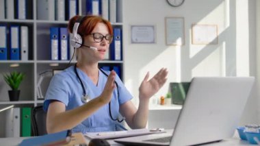 Çevrimiçi tıpta, genç bir kadın doktor, kulaklık kullanarak bilgisayar üzerinden video konferans yoluyla iletişim kuruyor, test sonuçlarını hastane ofisinde otururken anlatıyor.