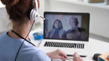 İnternet tıbbı, mikrofon ve kulaklık kullanan kadın doktor, ofiste otururken yaşlı hastalara video konferansı yoluyla danışmanlık yapıyor.