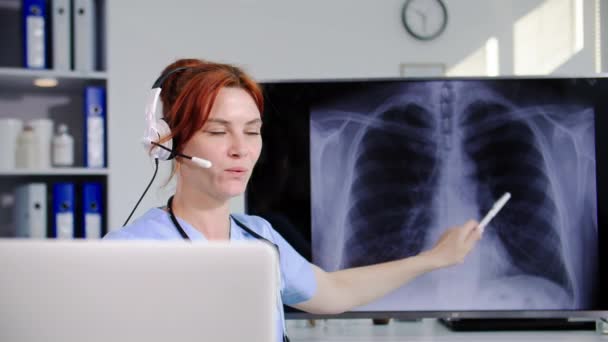 現代医学 若い女性医師はヘッドセットとビデオ通信を使用して患者に相談し オフィスに座っている間にX線の結果を示します — ストック動画