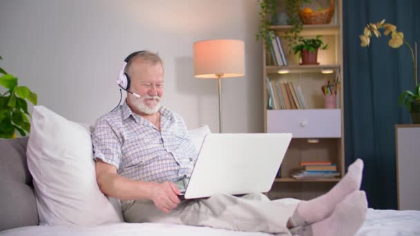 Elderly Man Lying Sofa Using Headset Communicates Video Communication Laptop — Stock Video