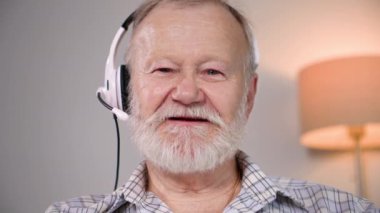 Çevrimiçi arama, modern emeklilerin bir video görüşmesinde konuştuğu bir kulaklık kullanarak rahat bir odada dinlenip kameraya bakması.