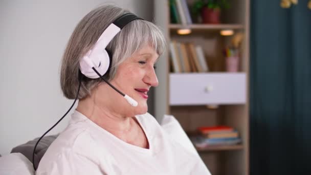 Hermosa Pensionista Femenina Utiliza Auriculares Con Micrófono Para Comunicarse Línea — Vídeos de Stock