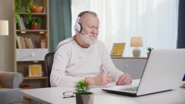 Kulaklık takan çekici, olgun bir adam rahat bir odada otururken bilgisayarla iletişim kuruyor.