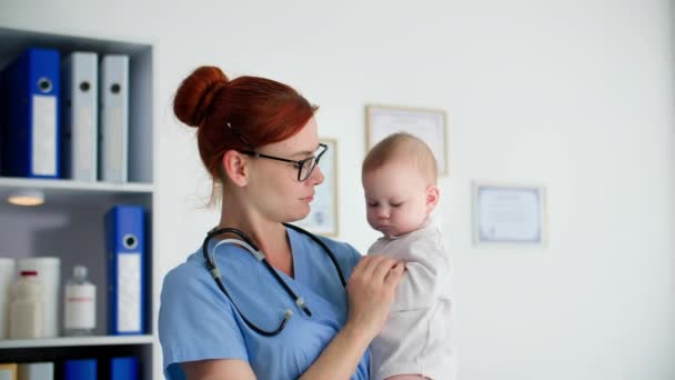 子供の健康 メガネをかけた小児科医 腕に小さな子供を抱え 患者が医療室にいる間 — ストック動画