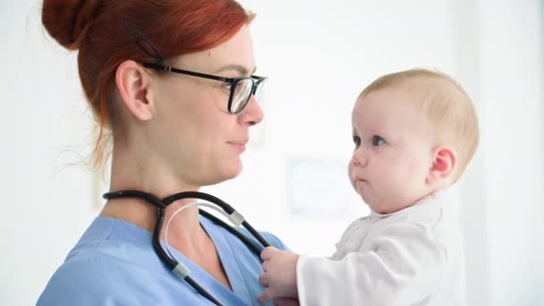 在医生办公室接待病人时 一个年轻女医生抱着幼儿的肖像 — 图库视频影像