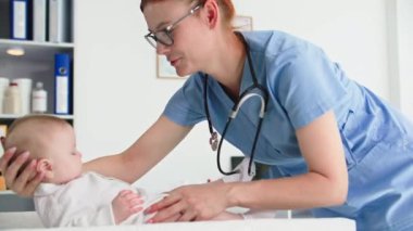 Bebek sağlığıyla ilgilenen, gözlüklü kadın çocuk doktoru, tıbbi muayenehanedeki küçük çocuğu muayene ediyor.