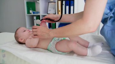 Doktor muayenesinde bebek bezli küçük bir kadın çocuk, tıbbi muayenede fonendoskop kullanarak bebek bezi masasında yatıyor.