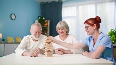 Yaşlı, neşeli kadın ve erkek emeklilerle ilgilenmek. Hemşire masada otururken masa oyunu oynamak eğlenceli.