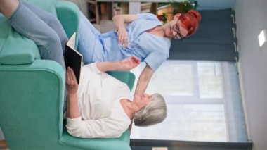 Yaşlı insanlarla ilgilenen, tıp üniformalı genç bir kadın, yaşlı bir kadına dikey ekranda bir bardak temiz su getiriyor.