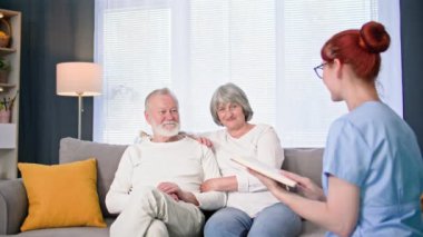 Yaşlı bir çiftle ilgilenmek, üniformalı bir kadın sosyal hizmet görevlisi, rahat bir odada yaşlı bir adam ve kadına kitap okumak.