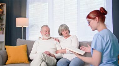 Yaşlılara sosyal yardım, odada yaşlı bir çifte kitap okuyan kadın sağlık görevlisi