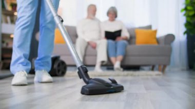 Yaşlıları önemsemek, elinde elektrikli süpürgeyle sağlık görevlisi olan sosyal hizmetler görevlisi yaşlı bir çiftin evi temizlemesine yardım ediyor.