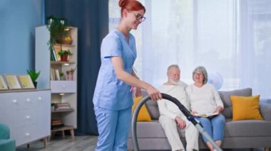 Elinde elektrikli süpürge olan kadın sosyal hizmet görevlisi yaşlı insanların evlerini temizlemesine yardım ediyor.